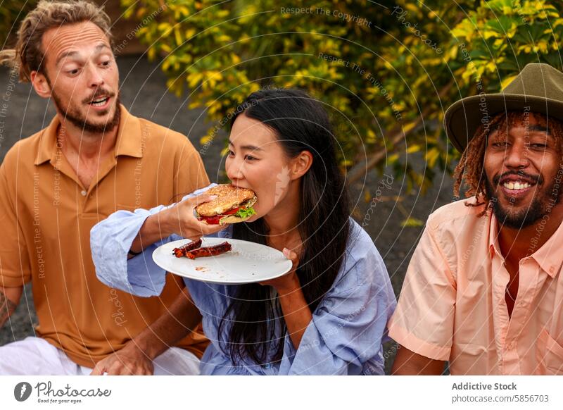 Freunde genießen eine Grillparty im Freien mit Musik und Essen grillen Burger multiethnisch asiatische Frau kaukasischer Mann afroamerikanischer Mann lässig