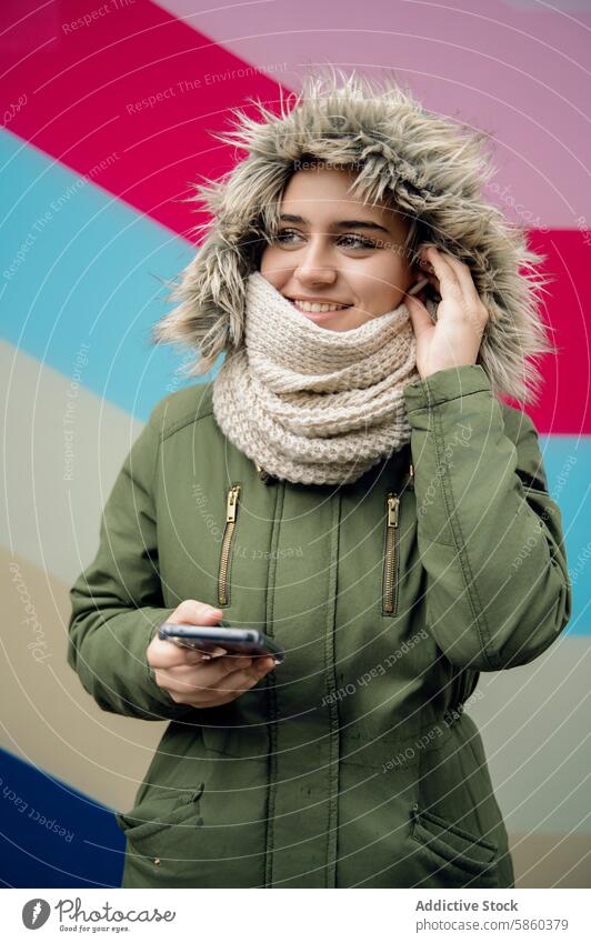 Junge Frau mit Smartphone auf buntem Hintergrund Winter Bekleidung Lächeln farbenfroh jung Erwachsener Technik & Technologie Handy Gerät Mitteilung