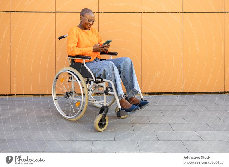 Afroamerikanische Geschäftsfrau im Rollstuhl mit Smartphone Frau Business Afroamerikaner schwarze Frau ethnisch lässig orange Jeansstoff Hintergrund heiter