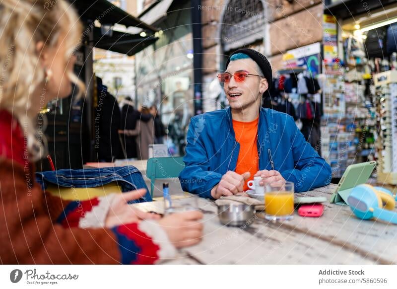 Junger Mann genießt einen Kaffee in einem Straßencafé in der Stadt jung im Freien Café Großstadt Lächeln digitales Gerät Buch urban Tisch blaue Haare