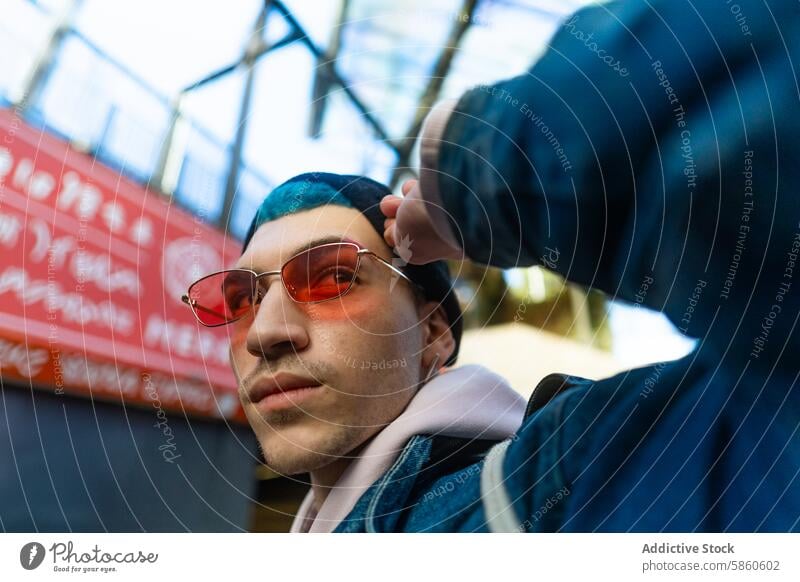 Stilvoller junger Mann mit blauem Haar und roter Sonnenbrille in städtischer Umgebung blaue Haare rote Sonnenbrille urban trendy stylisch Großstadt lässig