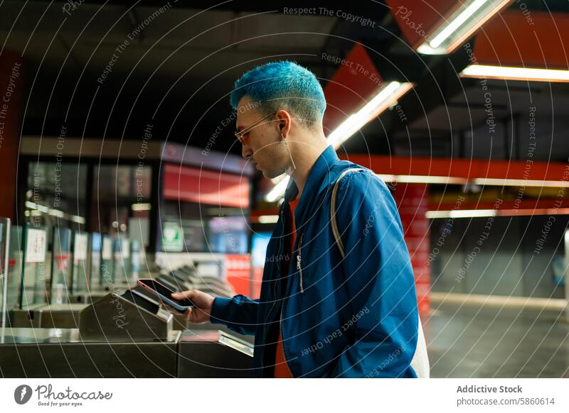 Junger Mann mit blauen Haaren liest Smartphone in einer U-Bahn-Station blaue Haare Stil Mode modern urban lesen Stehen jung Jacke Brille lässig allein Verkehr