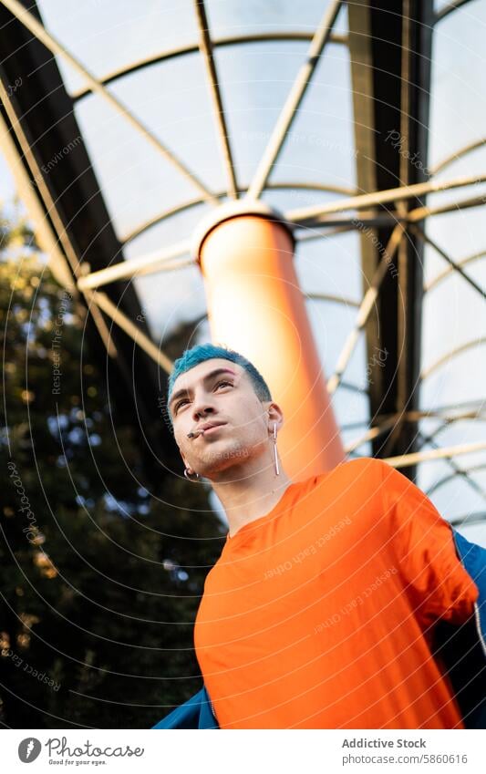 Junger Mann mit blauen Haaren in einem leuchtend orangefarbenen Hemd im Freien jung blaue Haare orangefarbenes Hemd modern stylisch geometrisch Architektur