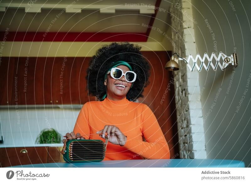 Retro-Foto einer fröhlichen schwarzen afroamerikanischen Frau mit einem alten Radio Afro-Look Sonnenbrille retro altehrwürdig orange Küche Tisch Glück Lächeln