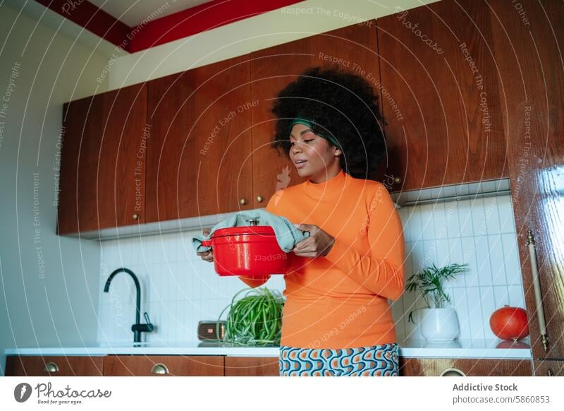 Schwarze afroamerikanische Frau in 50er-Jahre-Küche mit orangefarbenem Topf schwarz Afro-Look Essen zubereiten 1950s 50's altehrwürdig Mode herabsehend