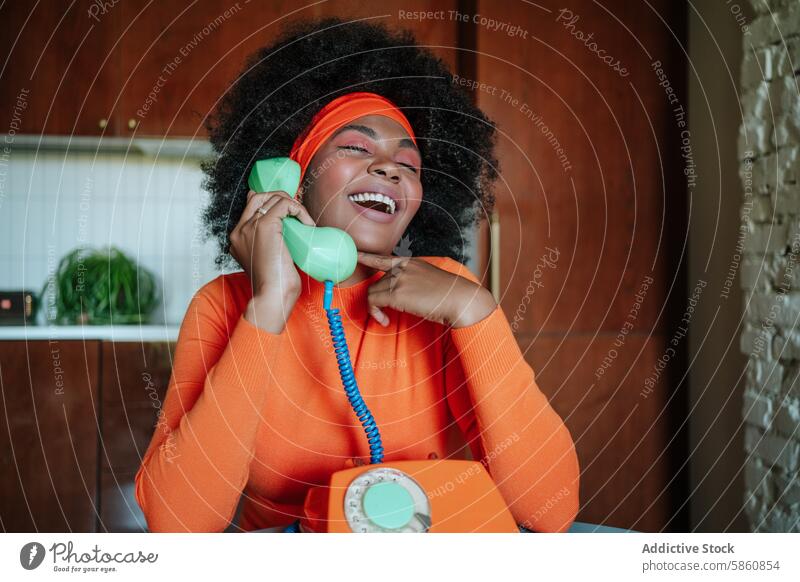 Fröhliche Hausfrau im Stil der 1950er Jahre plaudert am alten Telefon altehrwürdig 1950s freudig Küche orange schwarz Afroamerikaner Wegsehen Mode Nostalgie