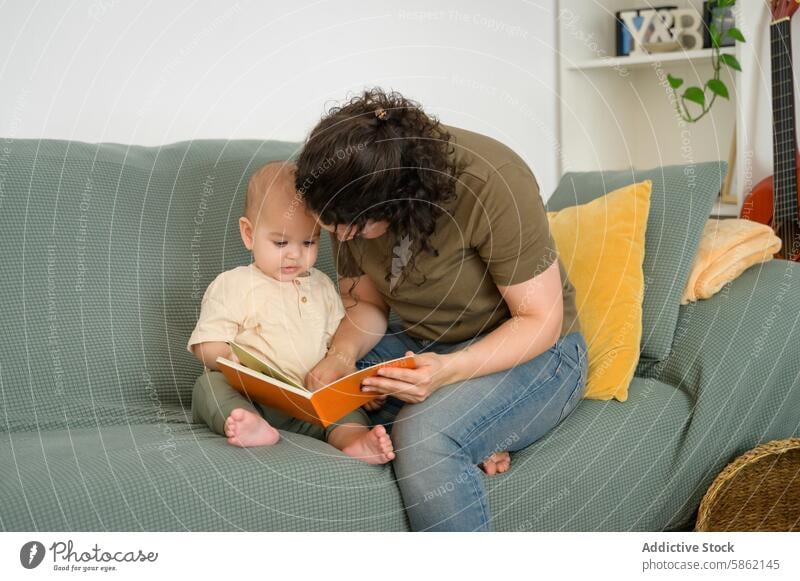 Mutter liest ihrem Baby auf der Couch sitzend vor lesen Buch Sofa Sitzen fokussiert Frau Kind im Innenbereich heimisch Bonden Familie Kindererziehung mütterlich