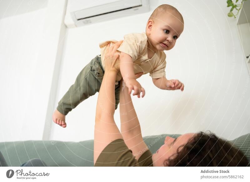 Anonyme freudige Mutter hebt lächelnden kleinen Jungen zu Hause in die Luft Baby Kaukasier Säugling Kleinkind Freude Spielzeit heimwärts Lächeln Bonden Pflege