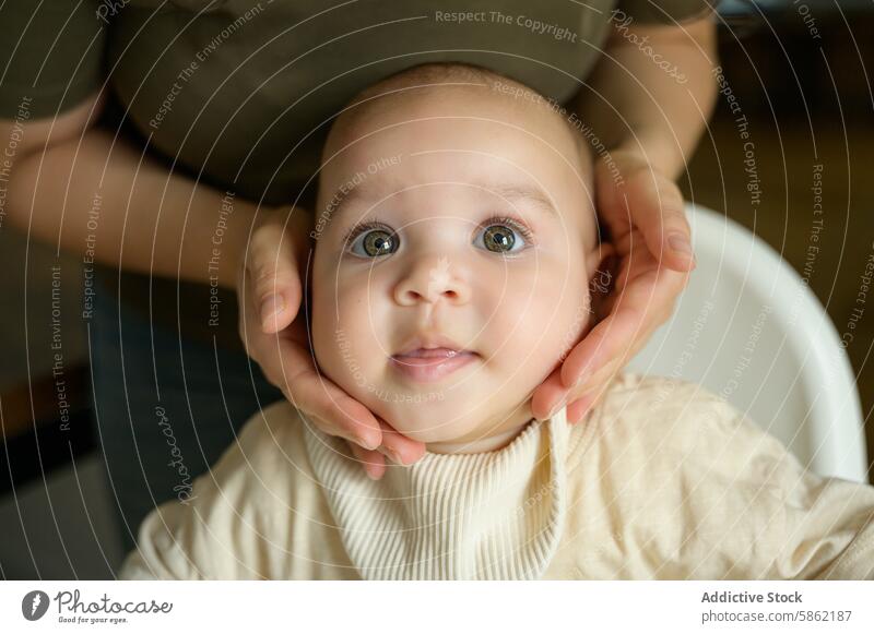 Baby mit grünen Augen, das von einem Elternteil gehalten wird und in die Kamera schaut Säugling grüne Augen Nahaufnahme Neugier Unschuld beigefarbenes Outfit