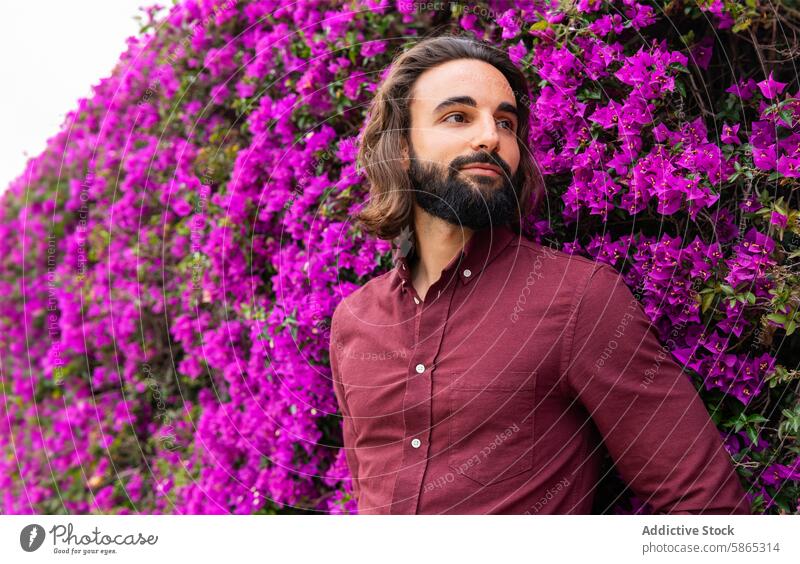 Mann in burgunderrotem Hemd posiert neben lebhaften lila Blumen purpur Bougainvillea Stil Gelassenheit Lifestyle Pose Burgunder Vollbart im Freien Natur Pflanze