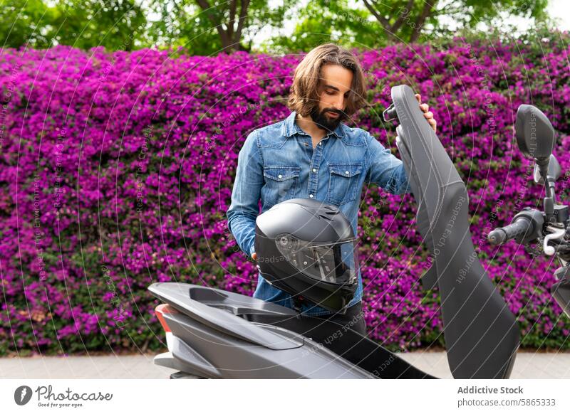 Mann bereitet sich auf eine Fahrt mit dem Motorroller in Poblenou vor Tretroller Schutzhelm Sicherheit im Freien Mitfahrgelegenheit Bougainvillea purpur Blumen