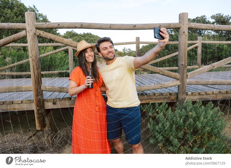 Freunde genießen ein Bier und machen ein Selfie im Freien lässig Sommer Frau Mann Brücke hölzern Natur Landschaft Flasche trinken Mobile Telefon Fotokamera Hut