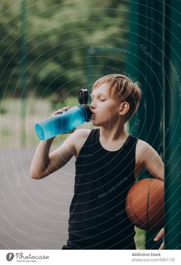 Junger Junge trinkt Wasser, während er im Freien einen Basketball hält Teenager Gericht jung sportlich Spiel Sommer Jugend Athlet aktiv Erholung Spielplatz