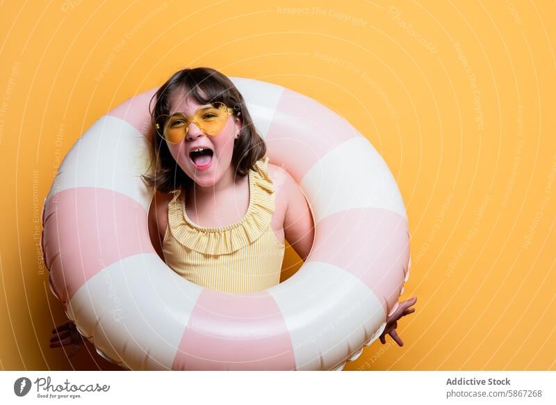 Fröhliches Kind mit Schwimmring in einem sommerlich gestalteten Studio Atelier Sommer Thema freudig Mädchen Sonnenbrille Badeanzug gelb Hintergrund