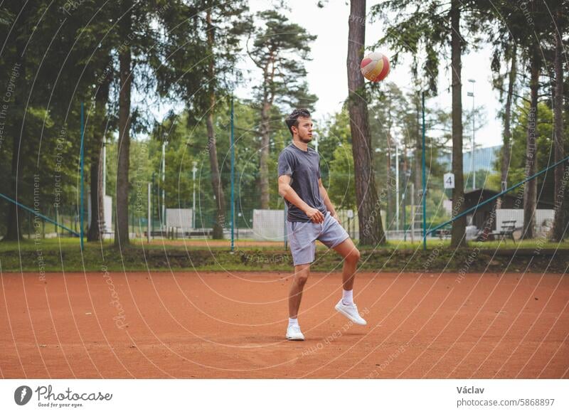 Fußballspieler in den 20ern spielt mit einem Luftballon auf einem Sandplatz. Amateursport. Individuelles Fußballtraining. Fußball. Kicken, Schlagen, Passen und Dribbeln