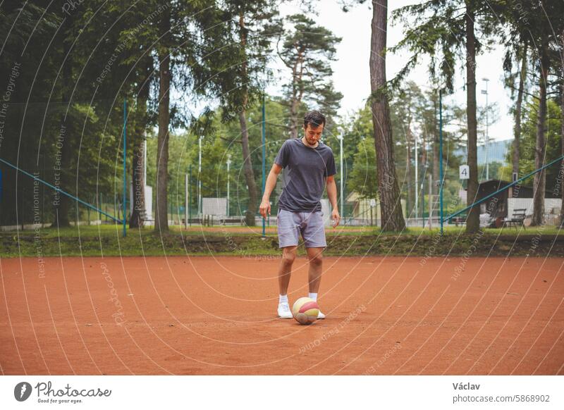 Fußballspieler in den 20ern spielt mit einem Luftballon auf einem Sandplatz. Amateursport. Individuelles Fußballtraining. Fußball. Kicken, Schlagen, Passen und Dribbeln