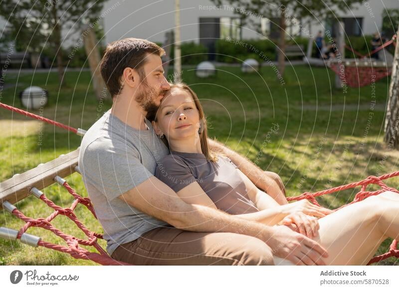 Paar entspannt sich gemeinsam in einer Hängematte im Park Mann Frau entspannend Sommer Komfort Zuneigung Starrer Blick Bäume im Freien Freizeit Fröhlichkeit