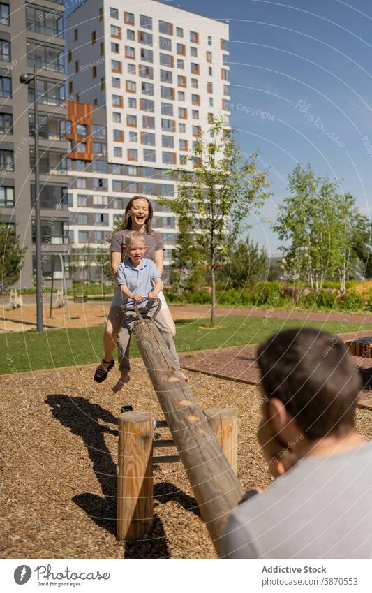 Die Familie genießt die gemeinsame Zeit auf einem Spielplatz im Park Mutter Vater Sohn Wippe Sommer spielen Freude Spaß im Freien Lächeln Wegsehen herabsehend