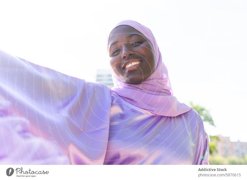 Gelassener Moment im Park mit einer lächelnden Frau im Hidschab Mutter Hijab freudig Lächeln sonnig im Freien spielerisch friedlich Lavendel Gewebe glühen