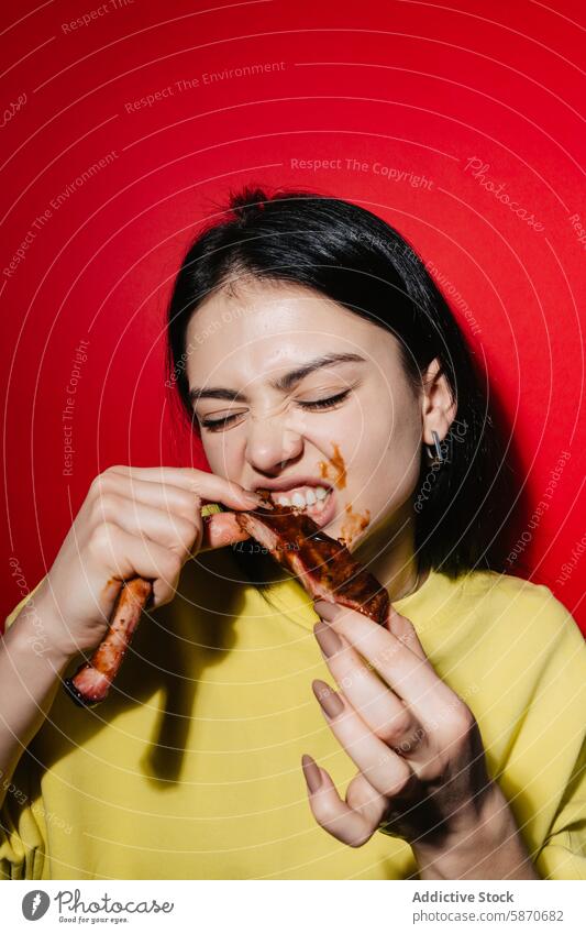 Junge Frau genießt unordentliche Grillrippchen vor rotem Hintergrund Barbecue Rippen Essen Saucen pulsierend gelb Hemd Lebensmittel Mahlzeit Genuss Vergnügen