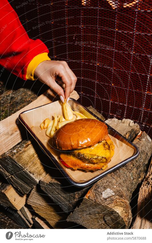 Burger und Pommes frites auf rustikalem Holzgestell beim Grillen braten Käse hölzern Platte Mahlzeit Barbecue gemütlich Person Hand packend Abendessen