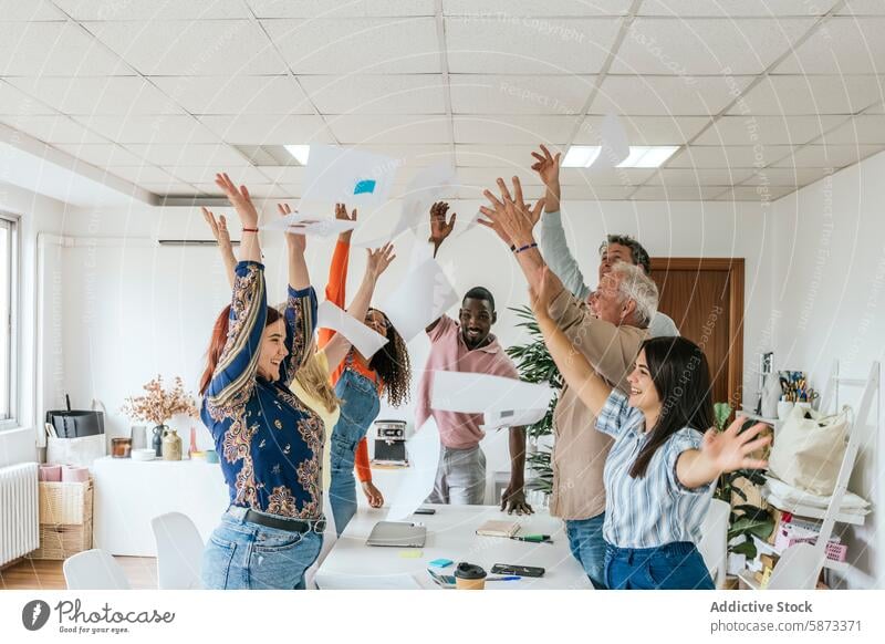 Ein buntes Team feiert den Erfolg in einem Coworking Space Feier professionell Papier Büro vielfältig multiethnisch rassenübergreifend Teamwork Werfen Air