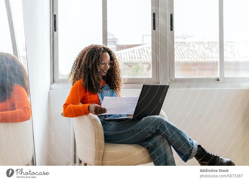 Afroamerikanische Frau arbeitet an einem Laptop in einem hellen Coworking Space Afroamerikaner Schriftstück Armsessel natürliches Licht Fenster Arbeit