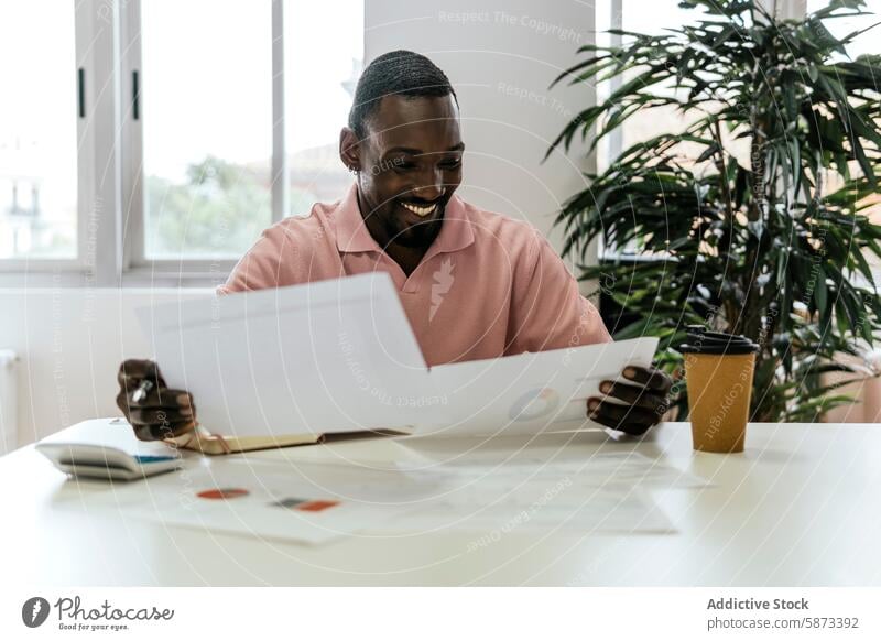 Ein afroamerikanischer Mann genießt seine Arbeit in einem hellen Büroraum Afroamerikaner Coworking Dokumente Papier Schreibtisch Kaffeetasse Arbeitsplatz Beruf