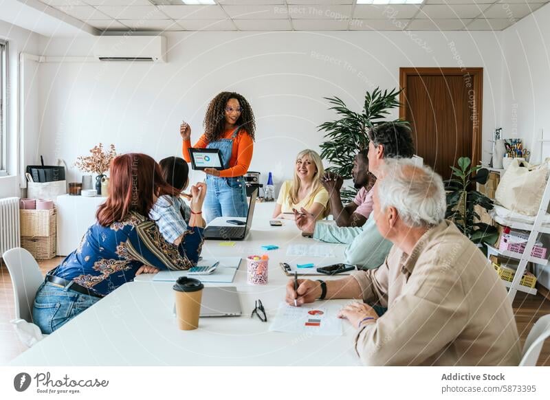 Vielfältiges Team, das sich in einem Coworking Space mit Technologie engagiert Büro Tisch Sitzen Stehen Präsentation Laptop Gerät Apparatur Teamwork