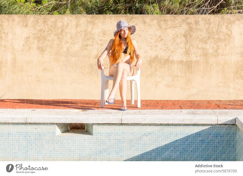 Junge Frau entspannt am Pool im Sommer entspannend Badeanzug Hut Freizeit sonnig Beckenrand Lifestyle jung rote Haare Sonne im Freien Urlaub Badebekleidung