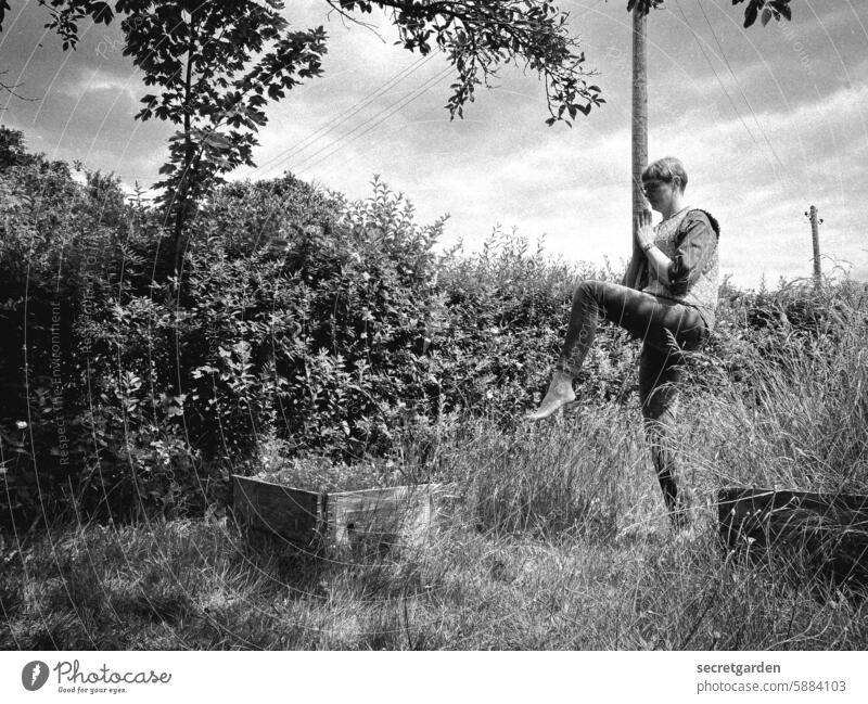 [HH Schregatour24] Einbeinige Königstauben-Pose Garten Yoga Schwarzweißfoto Humor lustig Frau Bein hebende Pfote einbeinig spielerisch Spielen Himmel Gras Hecke