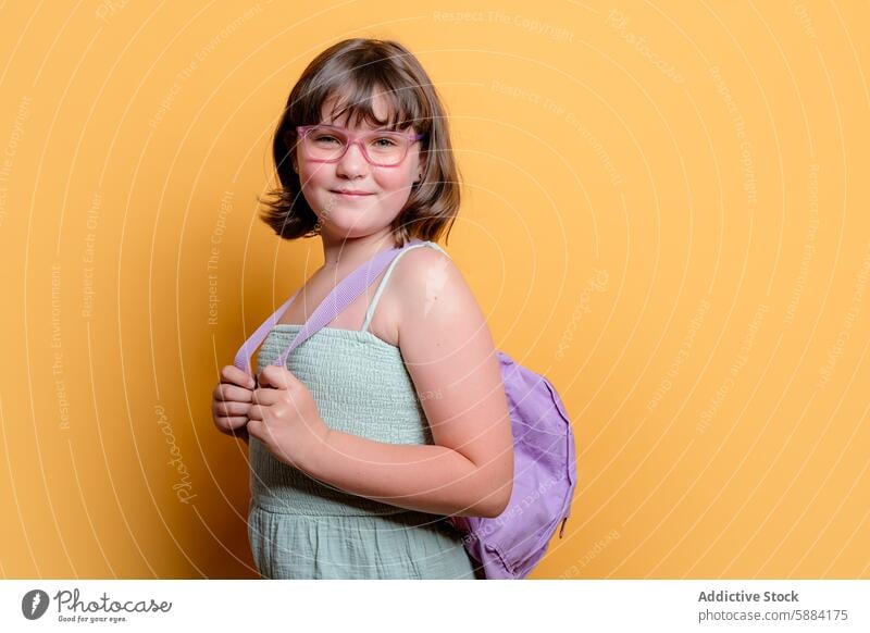 Schulmädchen mit Brille und Rucksack lächelnd im Studio Atelier Lächeln gelber Hintergrund Mädchen Pose Kind Schüler Bildung Glück Schule Accessoire Mode Outfit