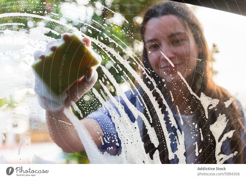 Frau lächelt beim Autoscheibenwaschen PKW Waschen Lächeln Sauberkeit Fenster Schwamm Seife Glas Wasser Tröpfchen Fröhlichkeit Autopflege Flugzeugwartung