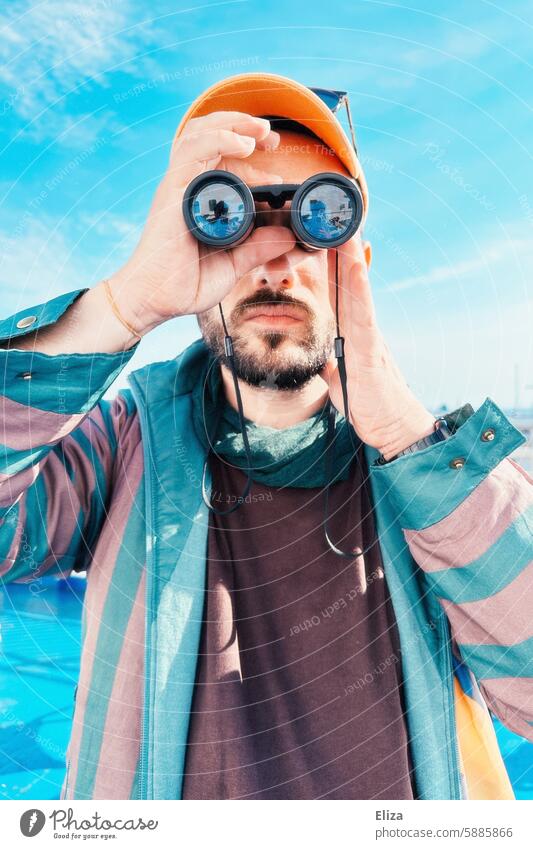 Mann beobachtet etwas durch ein Fernglas suchen erstaunt neugierig beobachten Mensch Hipster Blick entdecken Porträt bärtig modern blau grün Cap Schirmmütze