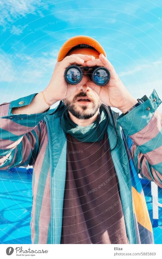 Mann beobachtet etwas durch ein Fernglas suchen erstaunt neugierig beobachten offener mund geschockt Mensch Hipster Blick entdecken Porträt bärtig modern blau