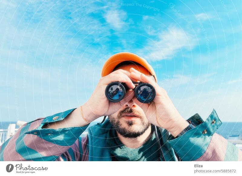 Mann beobachtet etwas durch ein Fernglas suchen erstaunt neugierig beobachten Mensch Hipster Blick entdecken Porträt bärtig modern blau grün Cap Schirmmütze