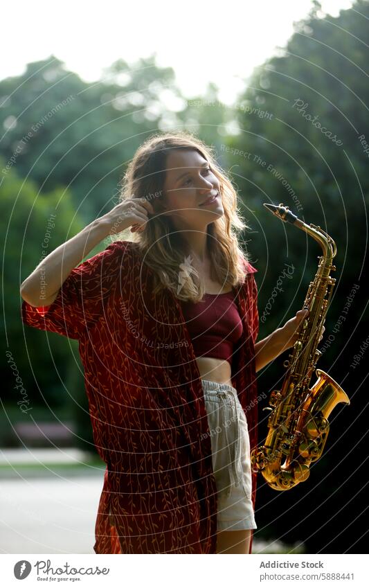 Junge Frau mit Saxophon in sonniger Parklandschaft Musik Musiker Sonnenlicht Sommer jung Kaukasier im Freien Freizeit Hobby Instrument Messing Saxophonist Natur