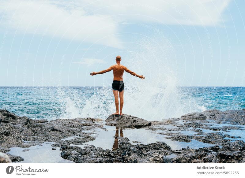 Mann stehend am felsigen Ufer mit plätschernden Ozeanwellen Sommer Feiertag Meer Spray Strand Felsen Arme Freude sonnig übersichtlich blau Himmel Natur Wasser