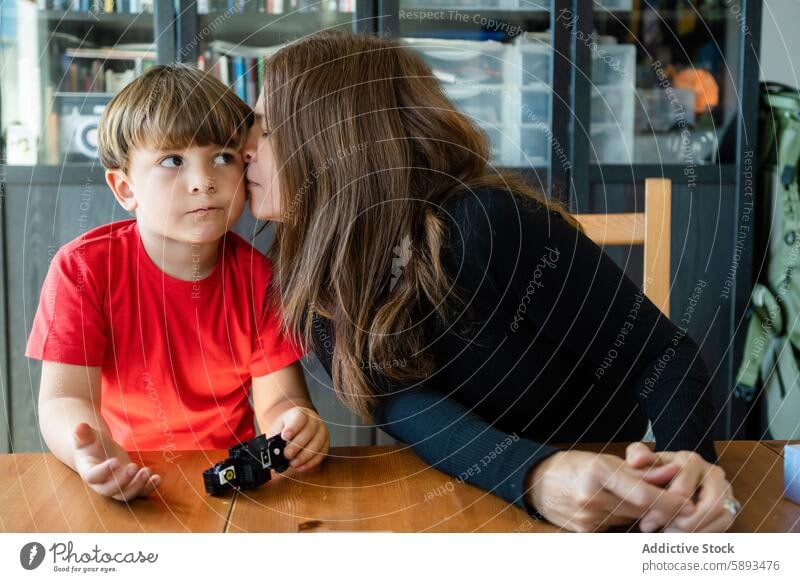 Liebevolle Mutter küsst süßen Sohn auf die Wange, während sie am Tisch sitzt Kuss spielen Spielzeug Bonden Zuneigung Partnerschaft Mama Mutterschaft Kindheit