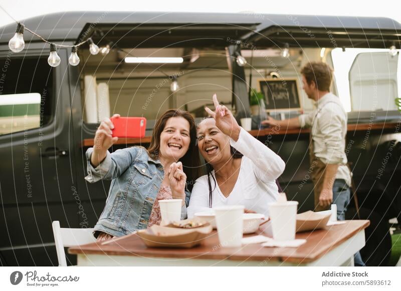 Erwachsene Frauen nehmen Selfie in der Nähe von Lebensmittel-LKW Lastwagen Glück Mittagessen Smartphone Zusammensein zwei Finger Lächeln v-Zeichen Optimist froh