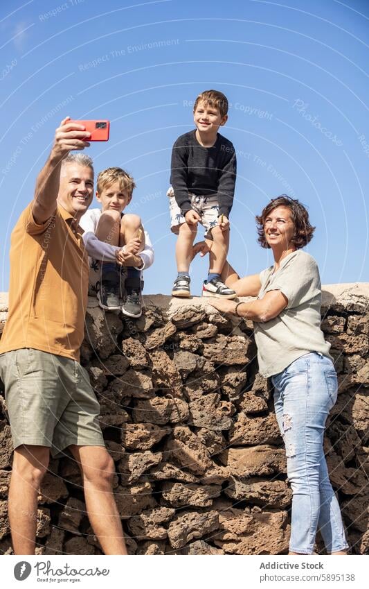 Glückliche Familie, die gemeinsam ein Selfie im Freien macht Sonnenschein Vater Lächeln Mutter Söhne Smartphone Zusammengehörigkeitsgefühl Bonden Freizeit Spaß