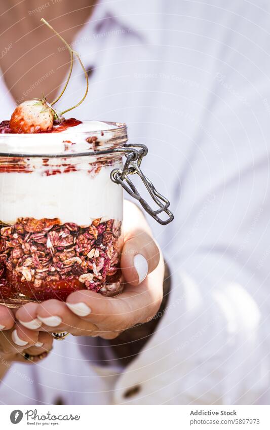 Nahaufnahme einer Hand, die ein Glas Joghurtparfait mit Müsli hält Frau Erdbeeren Frühstück Gesundheit Sommer Frucht Ebene nahrhaft Snack Haferflocken Beeren