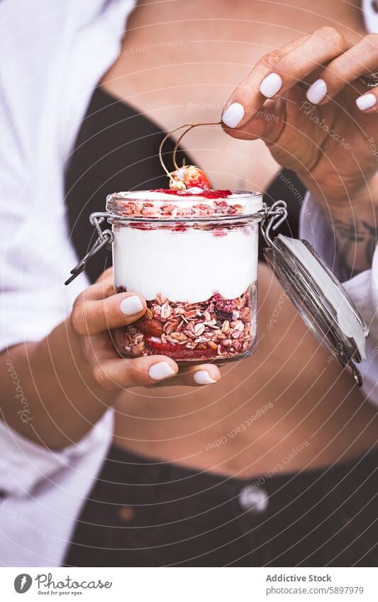 Frau hält ein Glas Joghurt-Parfait mit Früchten und Müsli Sommer Frühstück Gesundheit Erdbeeren Kirsche Hand unkenntlich anonym gesichtslos Ernährung frisch