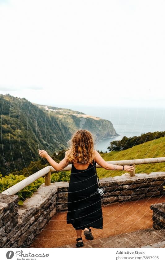 Frau umarmt landschaftliche Aussicht von Sao Miguel, Azoren. Rückansicht Aussichtspunkt São Miguel malerisch Küstenstreifen Klippe Meer ausgebreitete Arme