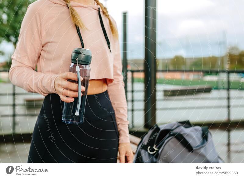 Junge Sportlerin mit Wasserflasche und Sporttasche Flasche unkenntlich Frau Athlet Mittelteil Hydratation Textfreiraum Top Beteiligung regnerisch Training