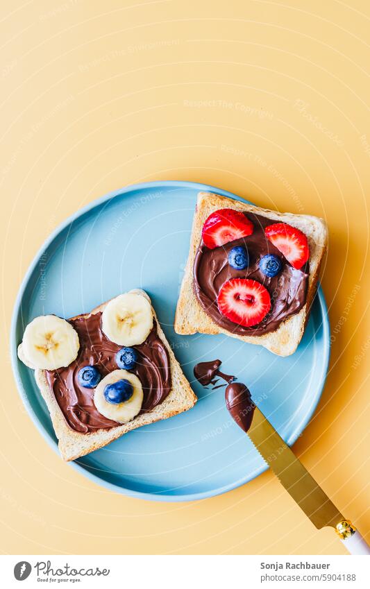 Zwei Toastscheiben mit Schokoladecreme und lustigen Tiergesichter aus Obst. Draufsicht. Frühstück Kind Toastbrot schokoladecreme Kindheit Teller