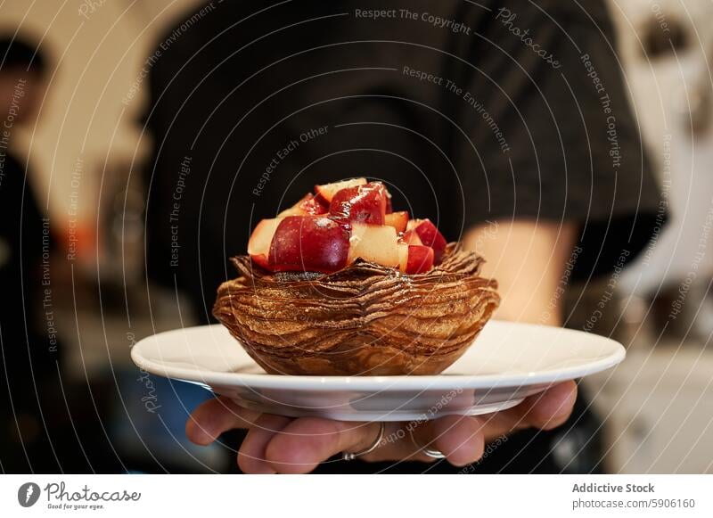 Nahaufnahme von Gebäck mit frischem Obst in der Hand eines Kellners unkenntlich anonym gesichtslos frisches Obst Servieren weiße Platte