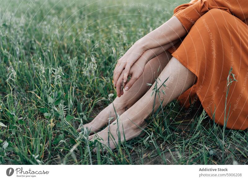 Beschnittene Ansicht einer Frau, die allein in einem grasbewachsenen Feld sitzt Gras Natur orange Kleid Sitzen unverhüllt Beine im Freien Ruhe Frieden Sommer