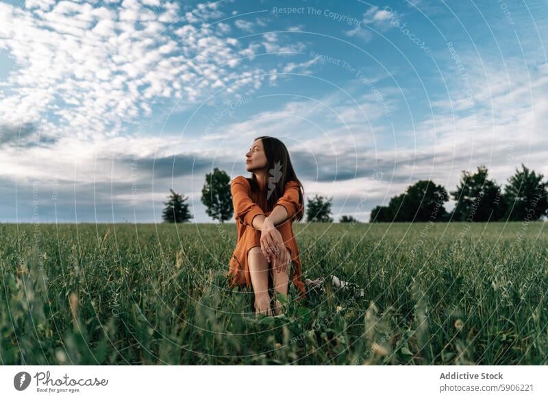 Gelassene Frau in orangefarbenem Kleid genießt die Natur in einem Feld Gelassenheit brünett orangefarbenes Kleid Wegsehen beschaulich im Freien grün Himmel