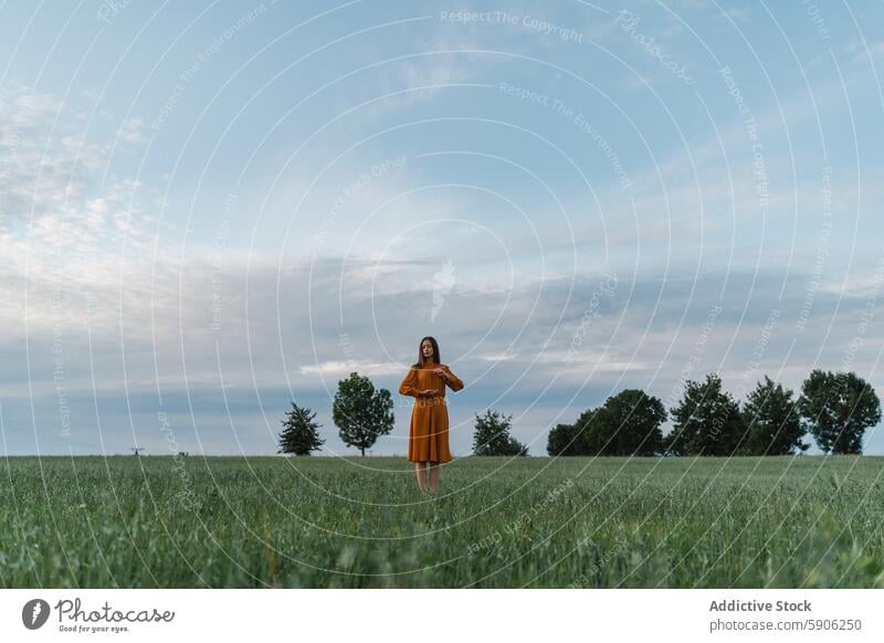 Frau in goldenem Kleid steht in üppigem grünen Feld unter bewölktem Himmel wolkig brünett Ruhe Natur Landschaft Gelassenheit im Freien Einsamkeit Sommer